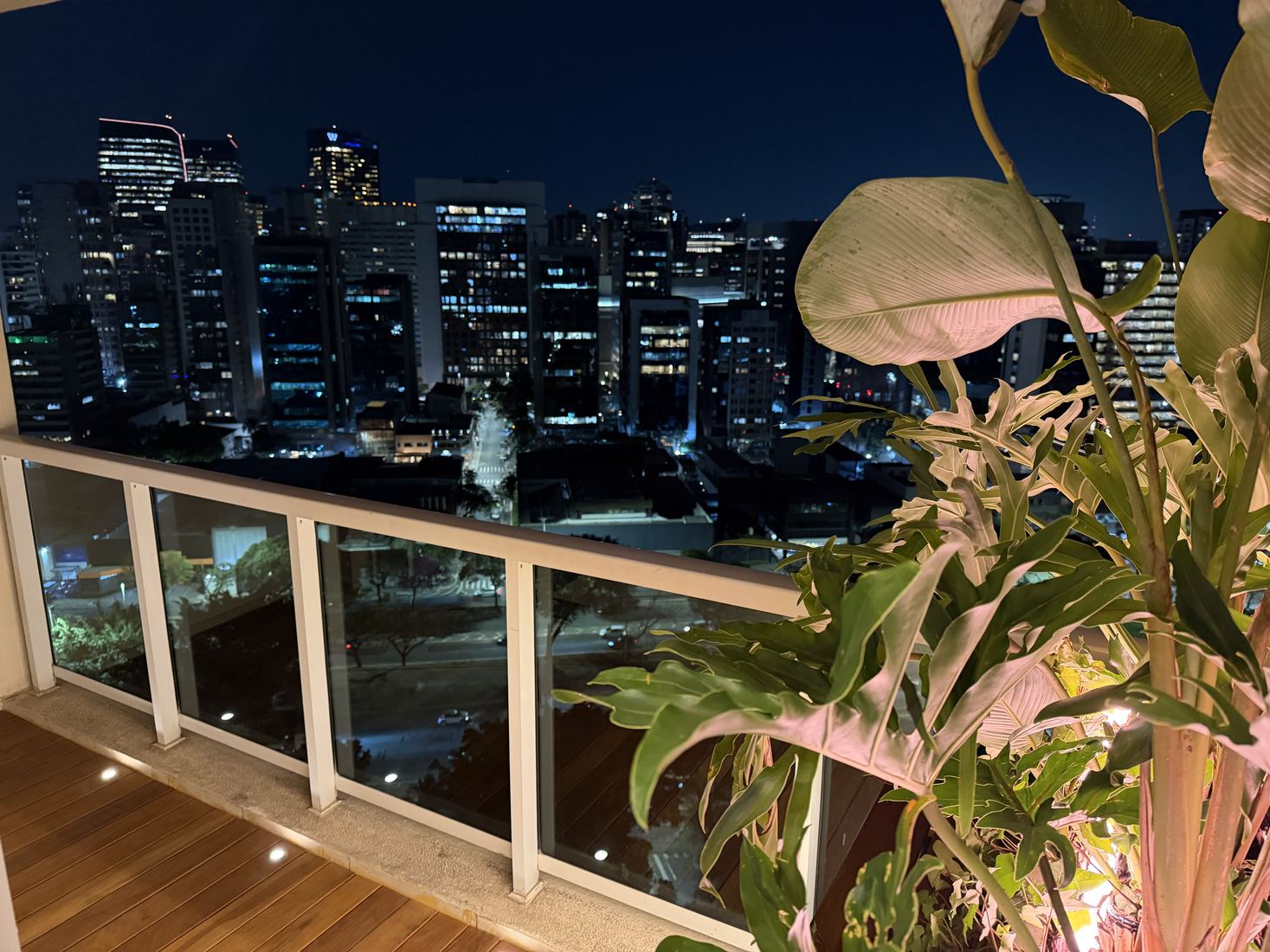 Varanda do centro de experiências à noite, com plantas e o skyline do Brooklin