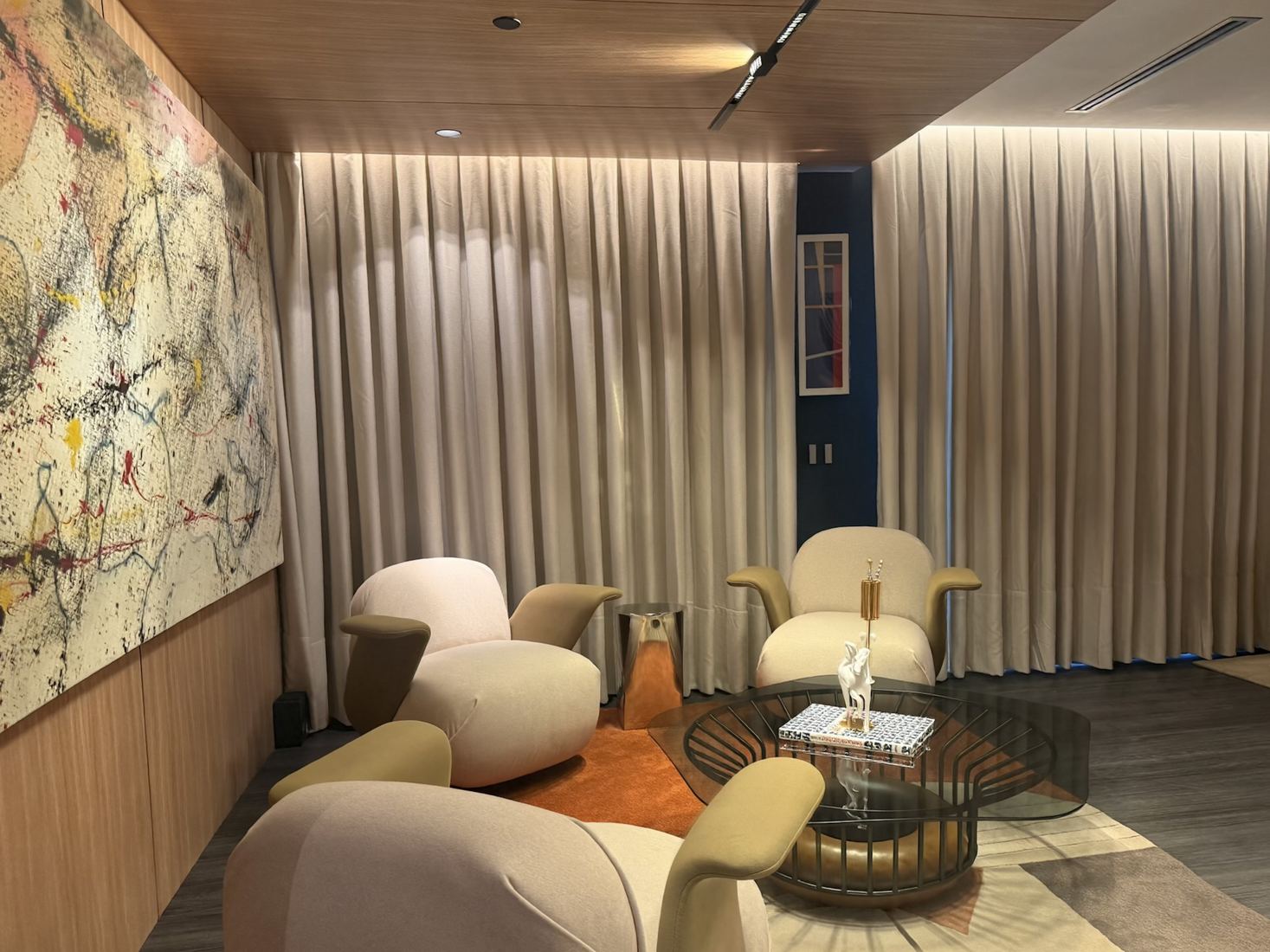 Estar do centro de experiências com poltronas, quadro abstrato e cortinas automatizadas